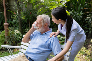 senior man happiness sitting with smiling nurse, takes care and discussion and cheer in the garden at nursing home