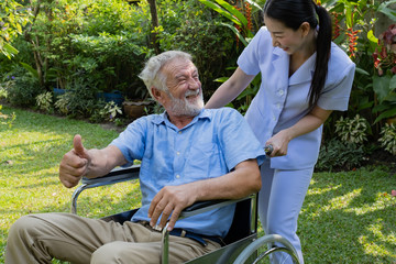 senior man happiness sitting on wheelchair with smiling nurse, takes care and discussion and cheer in the garden at nursing home