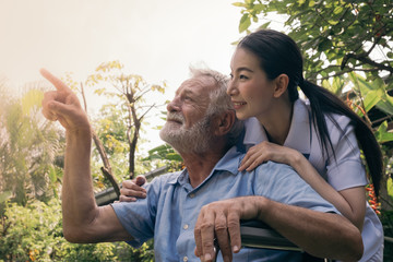 senior man happiness sitting on wheelchair and looking with smiling nurse, takes care and discussion and cheer in the garden at nursing home