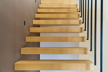 Floating stairs. Ash lumber stairs with railing attached to brown wall and leading to second floor...