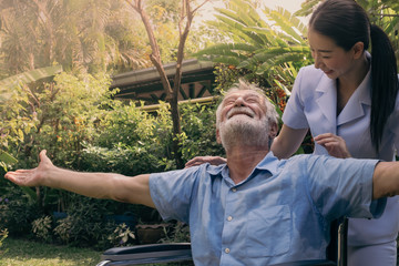 senior man happiness sitting on wheelchair with smiling nurse, takes care and discussion and cheer in the garden at nursing home