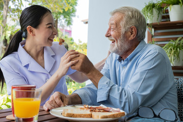 senior man happiness with smiling nurse, takes care breakfast at balcony near garden at nursing home