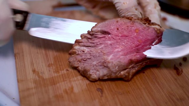 A close up shot of tri-tip meat being sliced or carved upon a wooden plank cutting board.