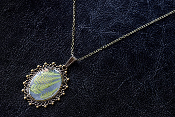 Fototapeta na wymiar Pendant made of epoxy resin and fern leaf on a dark background close up