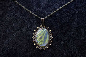 Fototapeta na wymiar Pendant made of epoxy resin and fern leaf on a dark background close up