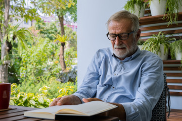 senior man happiness sitting and reading book at balcony near garden at nursing home for relaxing