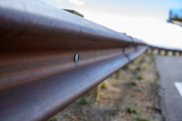 closeup of rusted metal guardrail along paved roadway 
