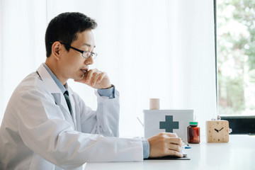 Asian male doctor sitting and hence to rest the chin on his hands and analyzes patient data. healthy lifestyle concept