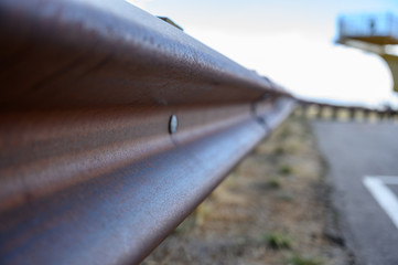 closeup of rusted metal guardrail along paved roadway 