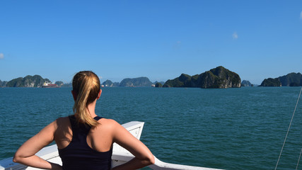 blonde woman on her back contemplates the scenery on a cruise ship sailing through halong bay, vietnam, south asia