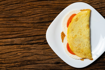 Crepioca. Pancake of cassava (tapioca) with cheese and tomato on plate on old wooden background. Selective focus.