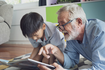 senior man happiness and grandson are sitting on the floor and playing games and reading book at living room together