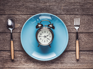 One vintage clock in blue ceramic dish with fork and spoon on wood table top view.