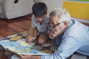 senior man happiness and grandson are sitting on the floor and playing games and reading book at...
