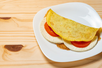 Casabe (bammy, beiju, bob, biju). Flatbread of cassava (tapioca) with caprese salad (tomato, mozzarella) on plate pinus wooden background. Selective focus.