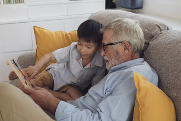 Obraz premium senior man happiness and grandson are sitting on the sofa and playing games and reading book at living room together