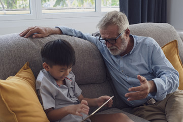 Fototapeta premium senior man happiness and grandson are sitting on the sofa and playing games and using tablet at living room together