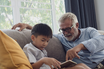 senior man happiness and grandson are sitting on the sofa and playing games and using tablet at...