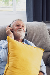 senior man happiness sitting on the sofa and listening music with headphone at living room for relaxing