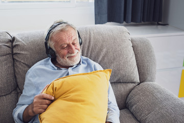Fototapeta premium senior man happiness sitting on the sofa and listening music with headphone at living room for relaxing