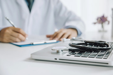 Stethoscope and Laptop on desk,Doctor working in hospital writing a prescription, Healthcare and medical concept