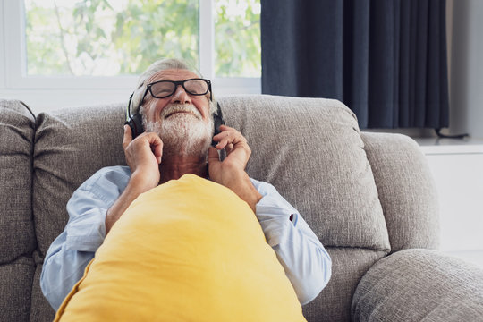 senior man happiness sitting on the sofa and listening music with headphone at living room for relaxing