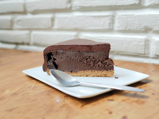 A piece of rich chocolate tart cake; with spoon served in white plate on wooden table. Selective focus.