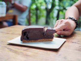 Cutting piece of rich chocolate tart cake; with spoon served in white plate on wooden table. Selective focus.
