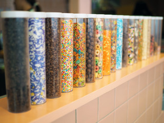 Row of rainbow colorful topping in plastic tubes with lid place on counter bar. Selective focus.