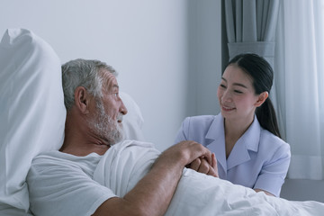 Obraz premium senior man with smiling nurse, takes care and discussion and cheer on bed at nursing home