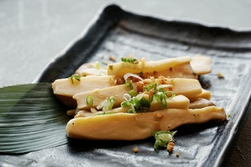 Selective focus of Stir fried mushrooms with butter sprinkled with scallion sliced in black plate on stone cutting board in restaurant, ready to eat or serve (Pleurotus Eryngii,King Oyster Mushroom)