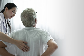 senior man back ache with smiling nurse, takes care and discussion on bed at nursing home