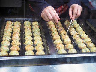 Making takoyaki which is a ball-shaped Japanese snack made of a wheat flour-based batter and cooked in a special molded pan. Japanese traditional snack.