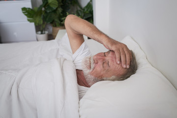 senior man sleeping alone and headache or dreaming nightmare on bed in room