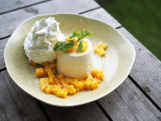 Yummy plate of Mango Panna Cotta with fresh mango and whipped cream on wooden table. Selective focus.