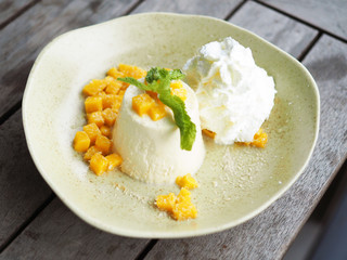 Yummy plate of Mango Panna Cotta with fresh mango and whipped cream on wooden table. Selective focus.