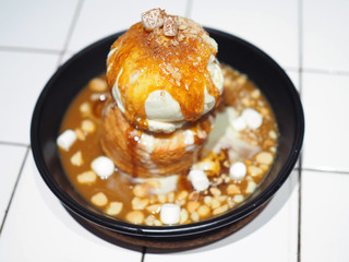 Croissant Doughnut or cronut top with scoop of vanilla ice cream and salty caramel, crunchy macadamia and marshmallow on hot pan. Selective focus.