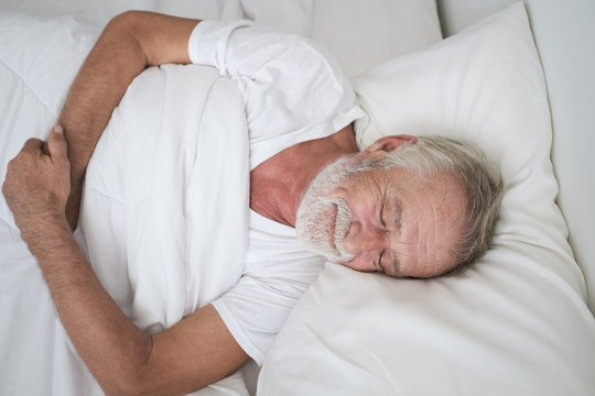 senior man sleeping alone and headache or dreaming nightmare on bed in room