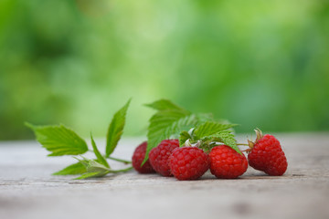 Ripe fresh sweet raspberries on wooden table with green garden background. Detox raspberry fruit for healthy living style.