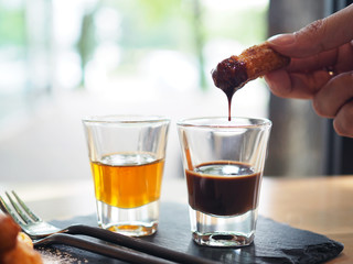 Dipping traditional Spanish dessert churros  with hot chocolate sauce serve on black stone tray.