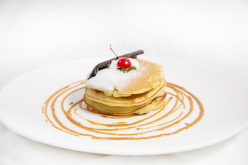 Pancakes topped with chocolate, icing sugar, and red cherry. Morning breakfast snack.