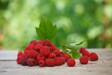 Pile of fresh Red raspberries with raspberry leaf on old wooden table, with green  blurred background. Healthy eating concept.