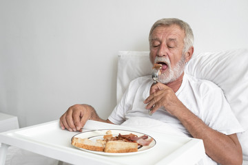 senior man with smiling nurse, takes care breakfast and discussion and cheer on bed at nursing home