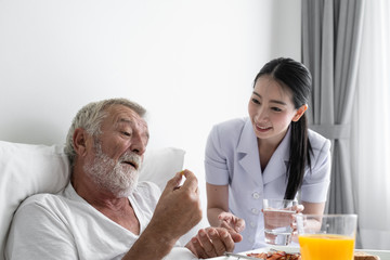 nurse give pill to senior man after breakfast and discussion on bed at nursing home
