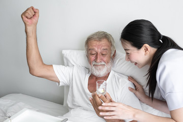nurse give pill to senior man after breakfast and discussion on bed at nursing home