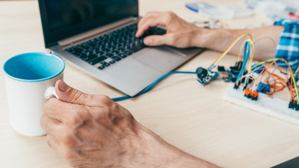 Programmer professional routine. Cropped shot of technician working at lab with laptop, drinking...