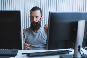 Tech support. Bearded software engineer using headset to receive call from customer.