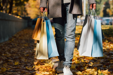 Autumn shopping. Cropped shot of man walking with bags along sidewalk covered with yellow leaves....
