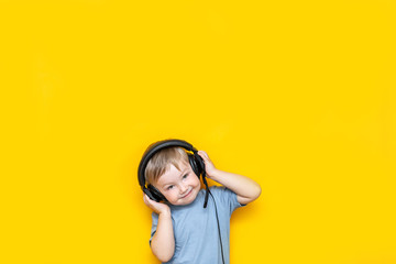 little cute caucasian blonde boy in headphones posing happy smiling isolated on yellow background