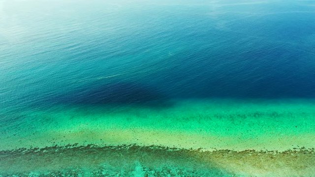 Aerial perspective above the Caribbean Sea. Shades of blue, turquoise and green with a revealed reef. Wide angle, dolly out.